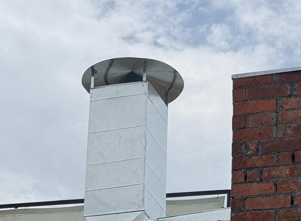 Chimenea de extracción con sombrero junto a muro de ladrillo